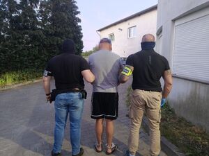 Dwaj funkcjonariusze prowadzą zatrzymanego mężczyznę zakutego w kajdanki.