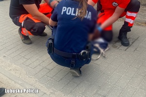 Policjantka i dwaj ratownicy medyczni kucają przy leżącej na chodniku kobiecie.