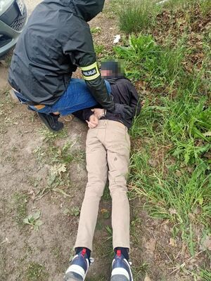 Policjant zakłada kajdanki zatrzymanemu leżącemu na ziemi.