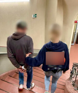 Zatrzymany mężczyzna jest prowadzony przez funkcjonariuszkę schodami w dół.