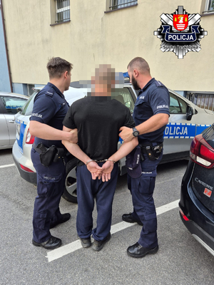 Dwaj policjanci prowadza zatrzymanego mężczyznę.