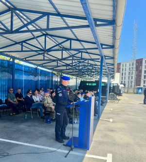 Funkcjonariusze XXXVIII rotacji JSPP w Kosowie i zaproszeni goście podczas uroczystości. Jeden z funkcjonariuszy stoi przy mównicy i przemawia do zgromadzonych.