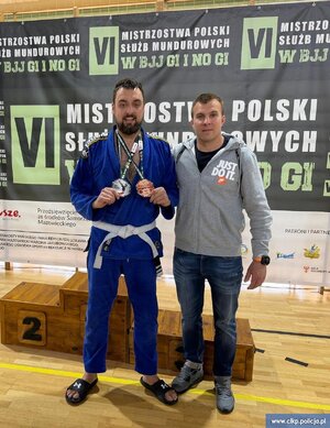 Podkomisarz Maciej Iwoła z Centralnego Laboratorium Kryminalistycznego Policji z innym zawodnikiem prezentuje dwa medale, które ma zawieszone na szyi.
