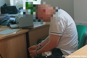 Mężczyzna w kajdankach siedzi na krześle przy biurku.