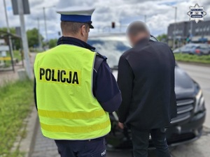 Policjant prowadzi zatrzymanego mężczyznę.