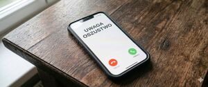 Leżący na stole telefon komórkowy a na jego ekranie widoczne połączenie przychodzące i napis: Uwaga oszustwo.