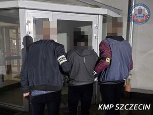 Dwaj policjanci wchodzą z zatrzymanym do budynku.