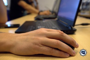 Na pierwszym planie dłoń na myszce komputerowej, w tle laptop.