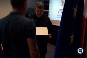 Funkcjonariusz Policji wręcza dyplom mężczyźnie.