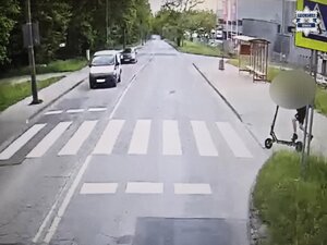 Stopklatka z nagrania monitoringu. Chłopiec z hulajnogą na przejściu dla pieszych. W stronę przejścia ulicą jadą dwa samochody osobowe.