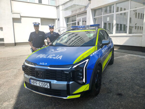 Dwaj policjanci stoją przy radiowozie.