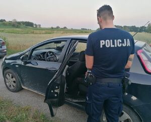Policjant stoi przy samochodzie, w którym siedzi odnaleziona starsza pani.