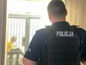 Na pierwszym planie odwrócony tyłem policjant patrzy na mężczyznę siedzącego w pomieszczeniu za kratami.