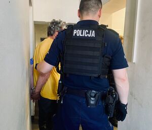 Policjant z zatrzymanym mężczyzna zakutym w kajdanki.