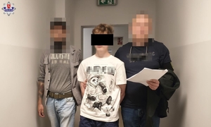 Dwaj policjanci prowadzą korytarzem zatrzymanego mężczyznę.