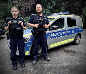 dwóch policjantów stoi przed radiowozem.