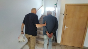 Zatrzymany mężczyzna prowadzony przez policjanta.