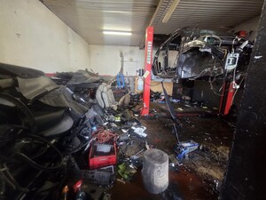 Wnętrze tzw. dziupli samochodowej. Po lewej stronie różnego rodzaju części samochodowe po prawej stronie częściowo rozebrany samochód na podnośniku.