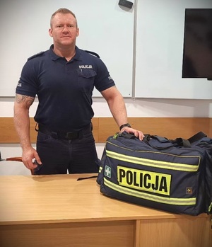 Umundurowany policjant, przed którym na stole lezy torba z napisem: Policja.