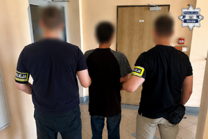 Dwaj policjanci trzymają zatrzymanego mężczyznę zakutego w kajdanki.