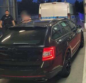 Na pierwszym planie samochód osobowy, który eskortowali policjanci. Za nim stoi radiowóz, a obok niego policjant.