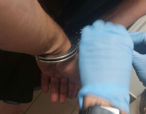Dłonie w rękawiczkach i zakładane zatrzymanemu kajdanki.