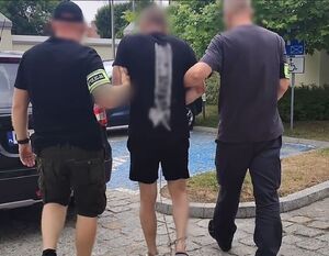 Nieumundurowani policjanci prowadzą zatrzymanego w zespolonych kajdankach.