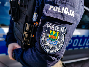 Policjant stoi bokiem, na jego ramieniu widoczna jest naszywka z napisem: Komenda Powiatowa Policji Hajnówka.