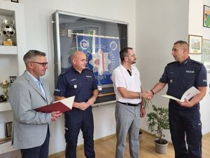 Policjant ściska dłoń mężczyźnie. Obok stoi drugi policjant i mężczyzna w garniturze.