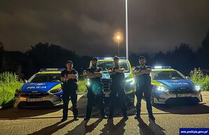 Policjanci: sierż. Paweł Sypytkowski, st. post. Kevin Stępiński, post. Adam Fiodorowicz oraz post. Patryk Godlewski stoją na tle radiowozu policyjnego.