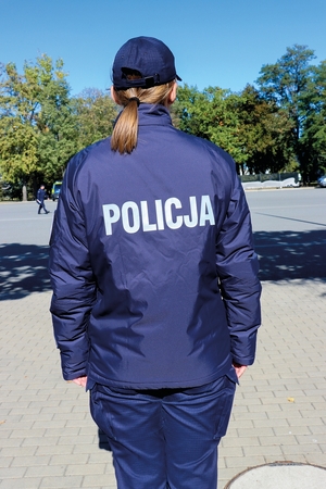 Odwrócona tyłem policjantka w nowym umundurowaniu. Na głowie ma czapkę typu bejsbolówka.
