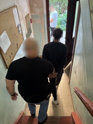 Policjant sprowadza do wyjścia z budynku schodami na dół mężczyznę.