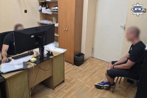 Zatrzymany mężczyzna siedzi na krześle podczas przesłuchania. Naprzeciwko siedzi przy biurku przesłuchujący go policjant.