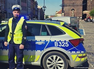 policjant stoi obok radiowozu.
