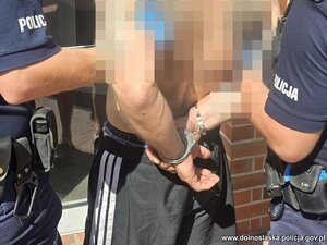 Zatrzymany w kajdankach na rękach, prowadzony przez policjantów.
