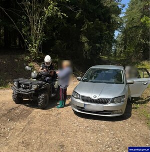 Policjant na quadzie, stojący obok mężczyzna i auto na leśnej drodze.