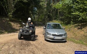 Policjant na quadzie i auto na leśnej drodze.