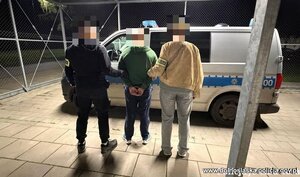 Dwaj policjanci prowadzą zatrzymanego do radiowozu.
