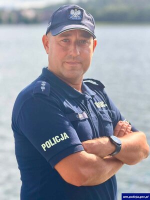 asp. szt. Łukasz Banaś – Zastępca Naczelnika Wydziału Prewencji Komendy Powiatowej Policji w Mrągowie na tle jeziora.