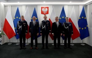Szef Europolu w towarzystwie komendanta głównego Policji, zastępcy komendanta głównego Policji i inny policjantów pozuje do zdjęcia na tle flag Polski i Unii Europejskiej.