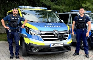 dwóch policjantów stoi obok radiowozu.