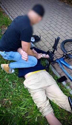 Policjant zakłada kajdanki mężczyźnie leżącemu na trawie.