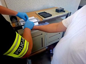 Policjant pobiera od zatrzymanego odciski palców.
