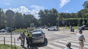 Policjanci ruchu drogowego przy radiowozie na rondzie, przy nich stoi mam z córką.