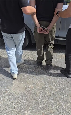 Zatrzymany mężczyzna w kajdankach prowadzony przez dwóch policjantów.