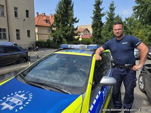 Policjant stoi przy radiowozie.