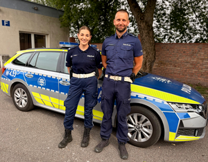 policjant i policjantka stoją przed radiowozem.