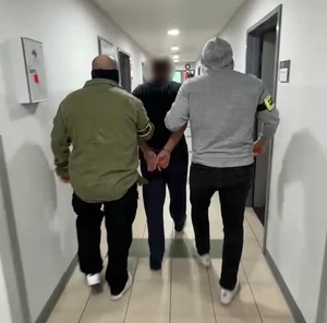 Dwaj policjanci prowadzą korytarzem zatrzymanego.
