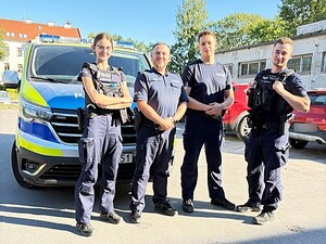 Czterech policjantów przy oznakowanym radiowozie.