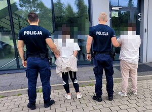 Dwaj policjanci trzymają dwie zatrzymane osoby.